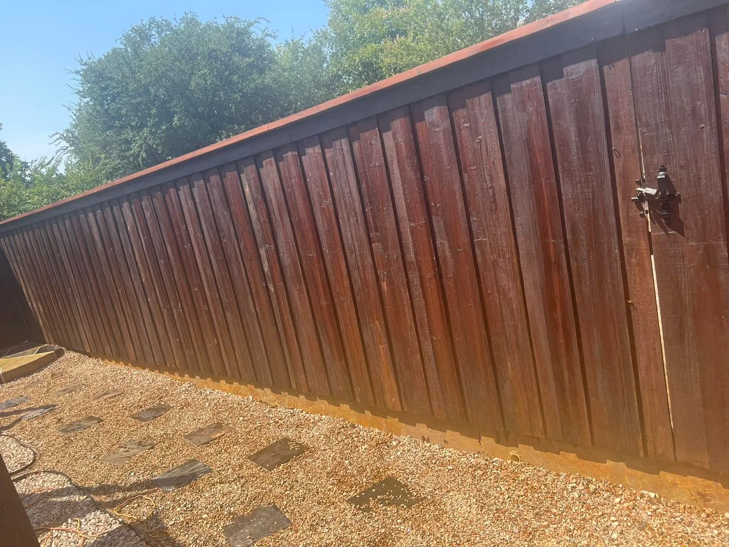 A long board-on-board cedar privacy fence finished in a rich red-brown stain, with a hardware latch on the gate